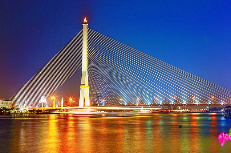 The illuminated Rama VIII bridge crossing the Chao Phraya river at dusk