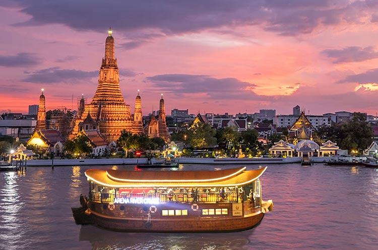 The wooden barge of the Arena Indian Dinner Cruise floating past Wat Arun on the Chao Phraya river