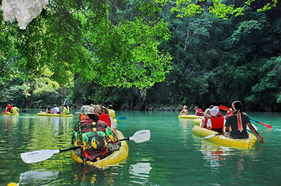 People in canoes paddling the emerald green waters of Phang Nga Bay