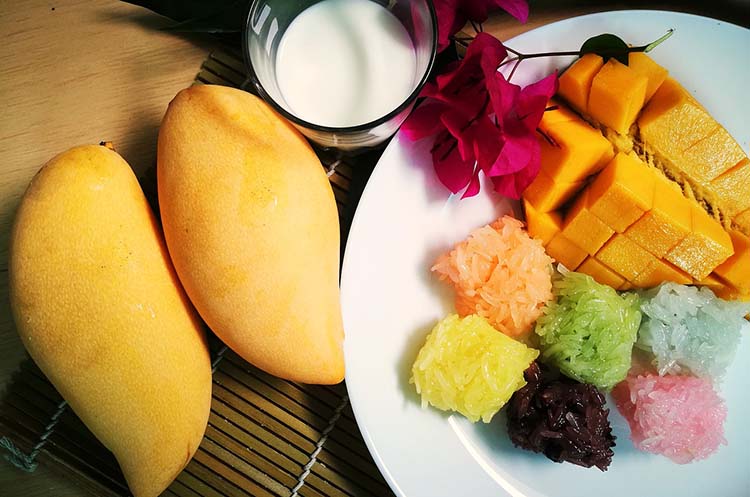 A plate with slices of mango and sweet sticky rice in various colors