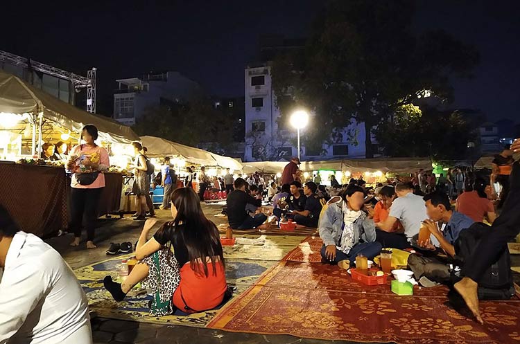 People squatting on mats eating Cambodian street food at the night market in Phnom Penh