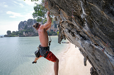 A rock climber on a steep rock over the beach