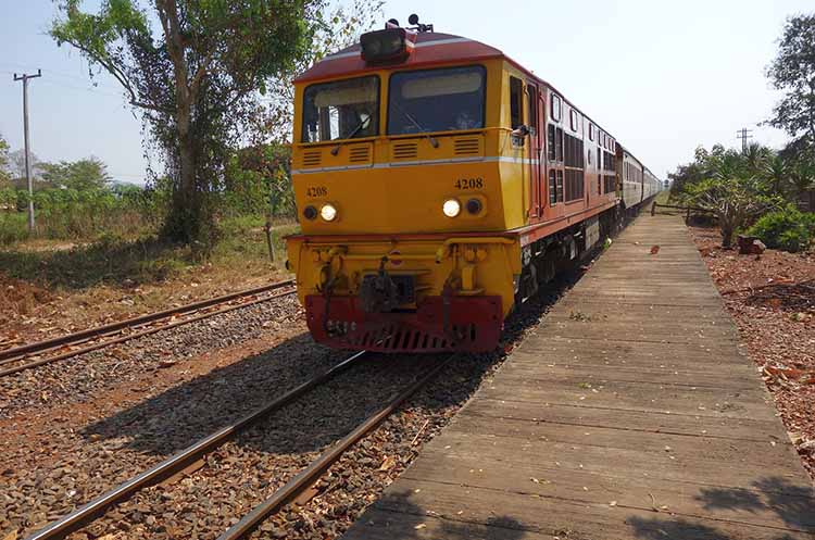 A passenger train at a small train station in rural Thailand